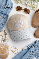 AMEN floral brim trucker hat flat lay with denim jacket boots sunglasses and iced coffee women’s boutique accessory