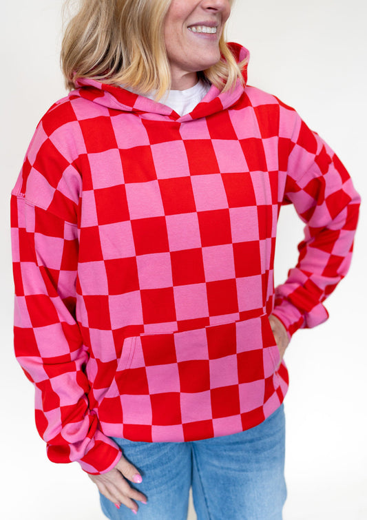 Person wearing a red and pink checkered hoodie against a white background. 