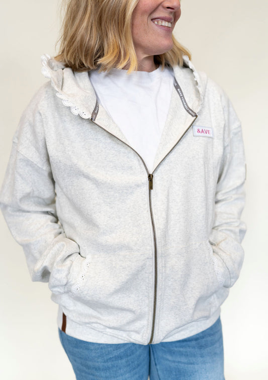 Person wearing a light gray hoodie with a brand logo and lace detail