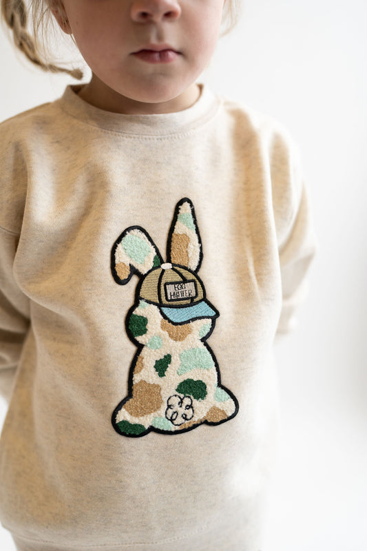 Child wearing a beige sweater with a chenille bunny patch camo design on a white background