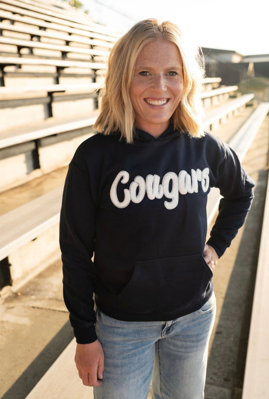 Show your school spirit in cozy style! This navy pullover hoodie features a bold&nbsp;Cougars chenille patch across the chest—perfect for chilly game nights, carpool mornings, or just repping your favorite team around town.

🧵 Details:

Classic navy hoodie with fuzzy white Cougars chenille patch

Soft fleece-lined interior for ultimate comfort

Front kangaroo pocket for chilly hands or game day snacks

Unisex fit—true to size with a relaxed silhouette

Available in sizes S through XL

