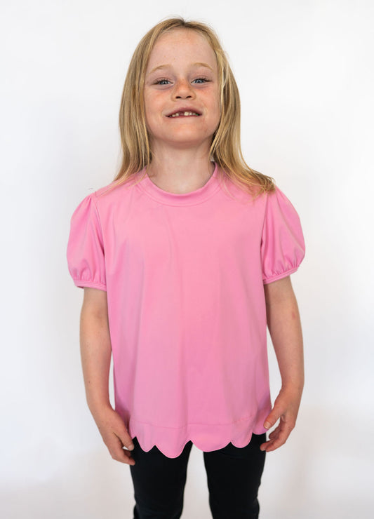 Lovely pink shade for a cheerful pop of color

Scalloped hem for a fun, feminine touch

Short puff sleeves with elastic cuffs

Soft, stretchy fabric for comfort and movement

Mix and match with leggings, shorts, or skirts

Available in toddler &amp; youth sizes 2T–9/10