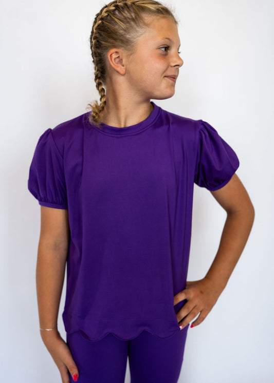 Gorgeous deep purple color for a vibrant pop

Adorable scalloped hem for a girly touch

Short puff sleeves with elastic cuffs

Soft, stretchy fabric for comfort all day long

Perfect for pairing with leggings, jeans, or skirts

Available in toddler &amp; youth sizes 2T–9/10