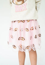 A child wearing a light pink tulle skirt with scattered metallic rose gold football-shaped sequins, paired with a cream sweatshirt against a plain white background.