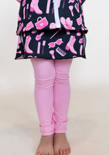Child wearing a dress with pink and black pattern and pink leggings on a white background