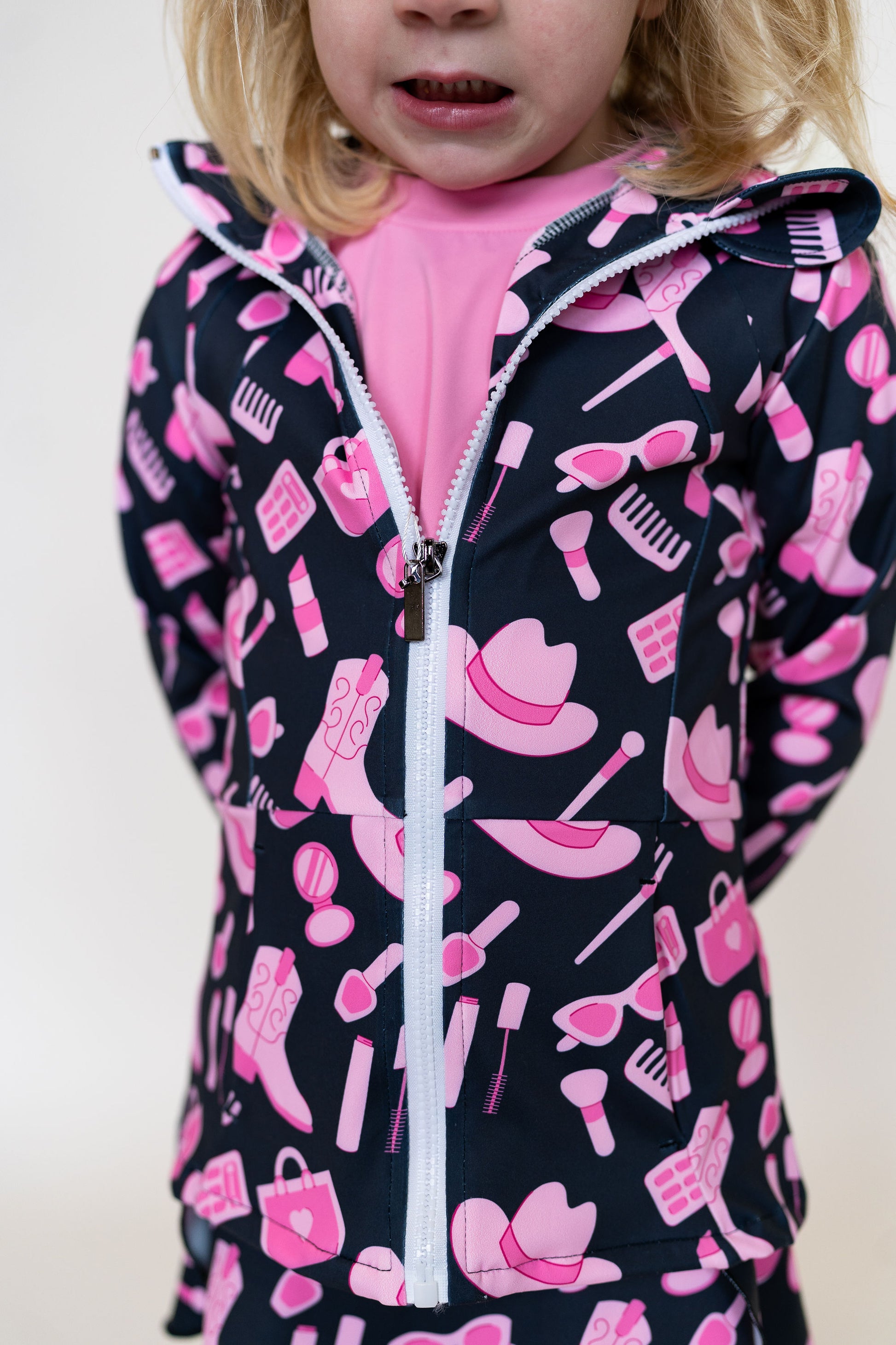 Child wearing a dark jacket with pink and white patterns on a plain background