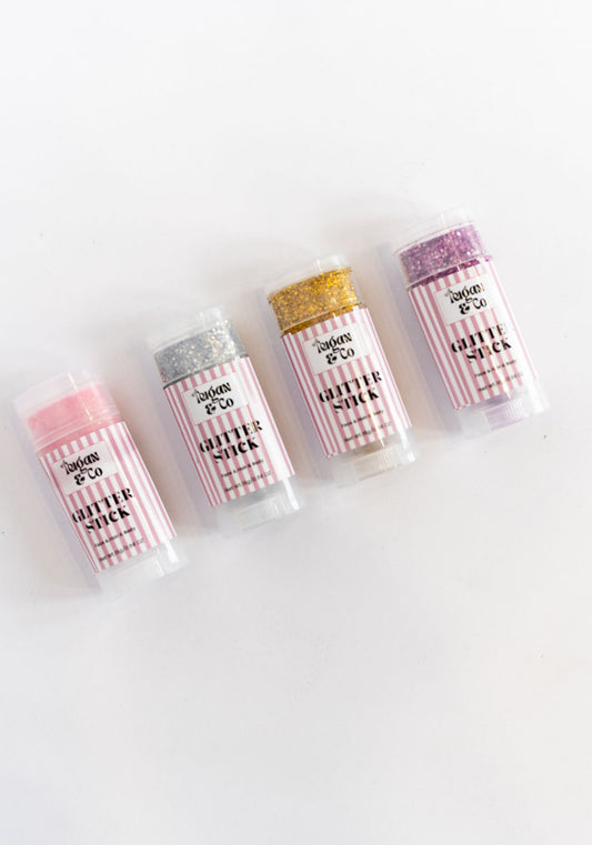 Five lip balm tubes with different colored tops on a white background Pink, Purple, Silver and Gold glitter sticks for hair and body
