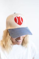 Women’s tan baseball hat with red heart baseball patch and blue striped brim, cute sporty cap for game day and everyday wear
