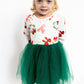 Young girl wearing a festive dress with red bows and green tulle skirt on a white background