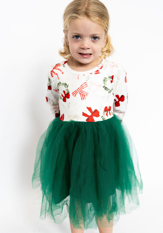 Young girl wearing a festive dress with red bows and green tulle skirt on a white background