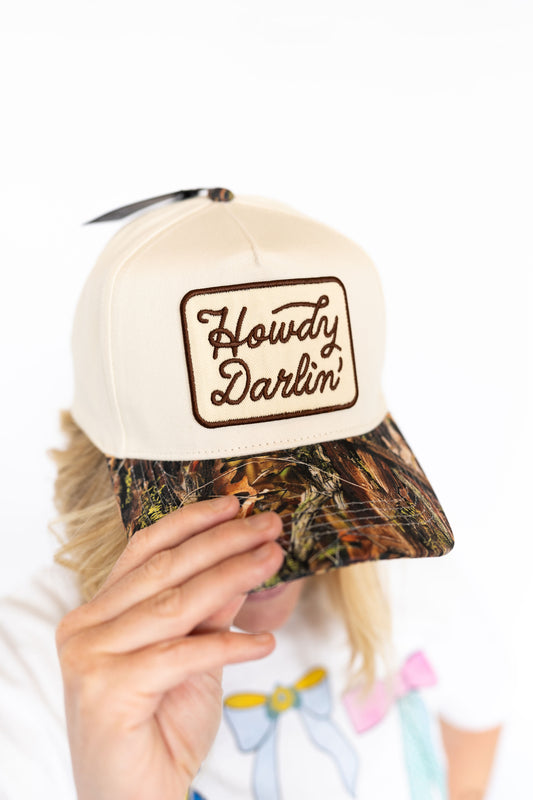 Classic structured trucker fit,
Cream front with embroidered “Howdy Darlin’” patch,
Camo print bill for extra southern spice, Adjustable snapback