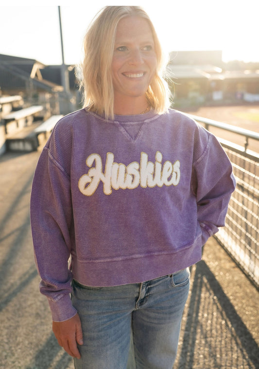 **Huskies Corded Crew: Purple Pride, Golden Spirit**

Show off your Husky pride with this irresistibly cozy purple corded crew! Designed with ultra-soft, mineral-washed fabric, it features standout white chenille lettering detailed with shimmering gold—because game days deserve a little glam! With its easy-going fit and vintage-inspired style, you'll be comfy and spirited all season long.

**Details:**

* Soft, mineral-washed purple corded fabric
* White chenille "Huskies" lettering with gold glitter outlin