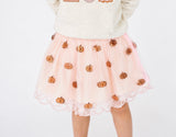 A child wearing a light pink tulle skirt with embroidered copper-orange pumpkins and a cream knit top, shown against a plain white background.