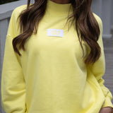 Person wearing a Terry cloth  yellow mock neck sweatshirt with a brand label " Lulu Mac"  on the chest.
