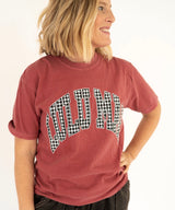 A woman wearing a faded red graphic t-shirt with 'LULU MAC' printed in an arched black-and-white houndstooth pattern across the chest, set against a plain white background.