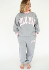 Model wearing the Lulu Mac Puff Mock Neck Sweatshirt in heather gray with oversized light pink LULU MAC lettering across the chest, a pink ribbed mock neckline, and matching pink cuffs. Styled with coordinating gray Lulu Mac joggers for a cozy matching set.