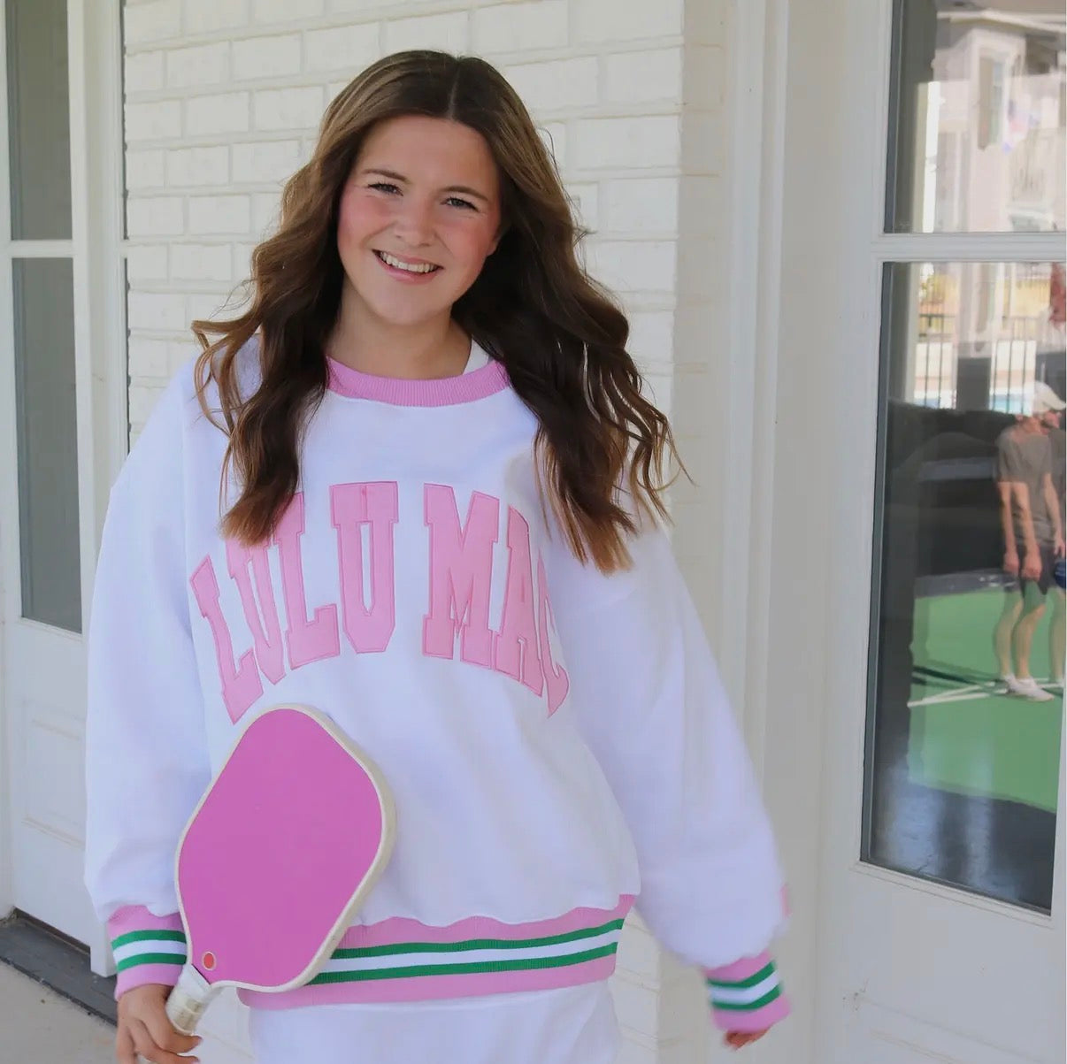 Person wearing a white sweatshirt with pink text that says Lulu Mac and white, green and pink varsity cuff and hem 