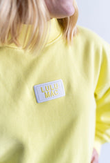 Close up of Lulu Mac Terry Cloth Mock Neck in yellow with embroidered logo patch on the chest