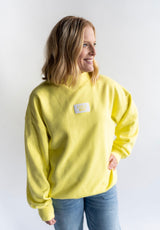 Women wearing Lulu Mac buttery lemon yellow mock neck sweatshirt. Terry cloth material with White and Yellow Logo on the chest
