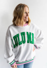 Woman wearing a white sweatshirt with 'LULU MAC" in green and pink, white and green striped cuff and hem  printed on it against a white background