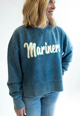 Person wearing a blue corded sweatshirt with 'Mariners' text from a chenille patch on a plain background