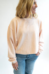 Woman wearing a pale pink corded crew sweatshirt  and blue jeans against a white background