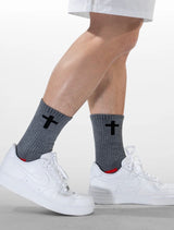 Gray socks with black cross design worn with white sneakers on a light background