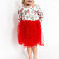 Young girl wearing a festive dress with a red skirt and patterned top on a white background