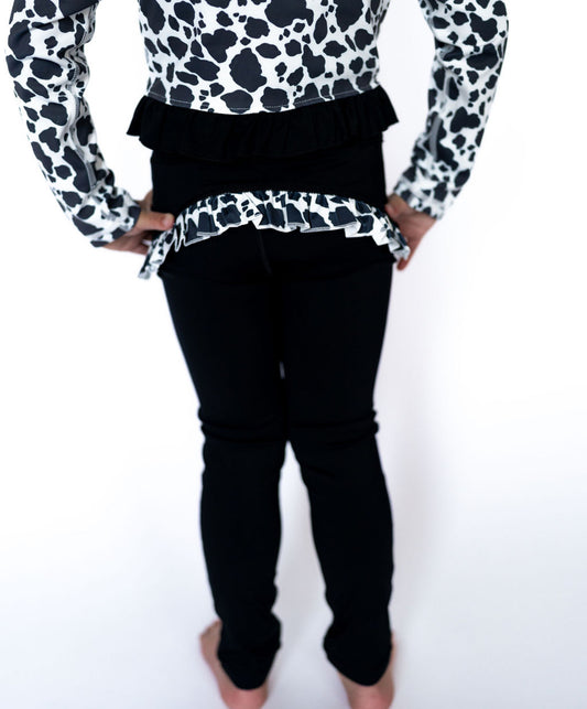 hese leggings are soft, stretchy, and designed for comfort, whether your little one is cartwheeling through the day or strutting into dance class with flair. Pair them with the matching cow print jacket for the full Teigan &amp; Co. statement set!

Details:

Black full-length leggings with stretchy waistband

Ruffle detail at the back in custom cow print

Soft, breathable athletic fabric perfect for play

Designed to move with your mini

Toddler + Youth sizing available

Pairs with our Cropped Cow Print Ath