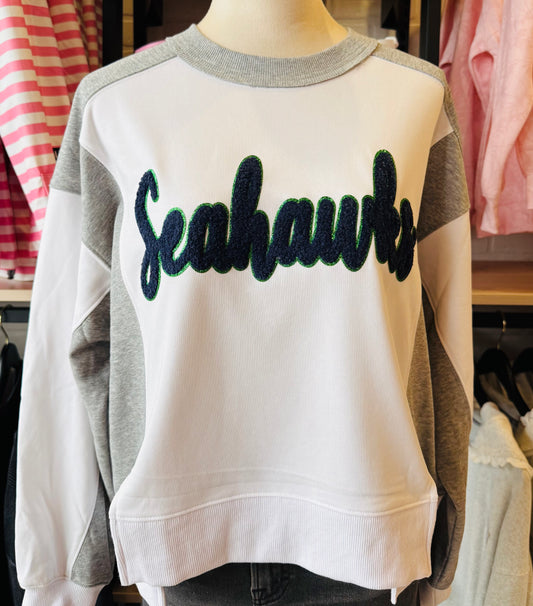White sweatshirt with 'Seahawks' chenille patch  text on a mannequin in a store setting.
