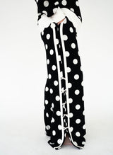 Simply Southern black wide-leg pants featuring oversized white polka dots, contrasting white side trim, decorative white bow accents along the outer legs, and side slits at the hems. Relaxed, full-length silhouette.