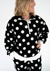 oman modeling a Simply Southern black quarter-zip pullover with oversized white polka dots, a white zipper, contrasting white cuffs, and a scalloped white hem. Relaxed fit with long sleeves.