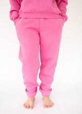 A person wearing bright pink Simply Southern sweatpants and a matching pink sweatshirt, shown from the waist down against a plain white background.