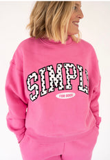 A woman wearing a bright pink Simply Southern sweatshirt with 'SIMPLY FOR GOOD' printed in white and black on the front, shown against a plain white background.