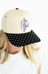 Cream and black Spartan mascot baseball hat featuring a purple Spartan patch and black brim with white polka dots.

