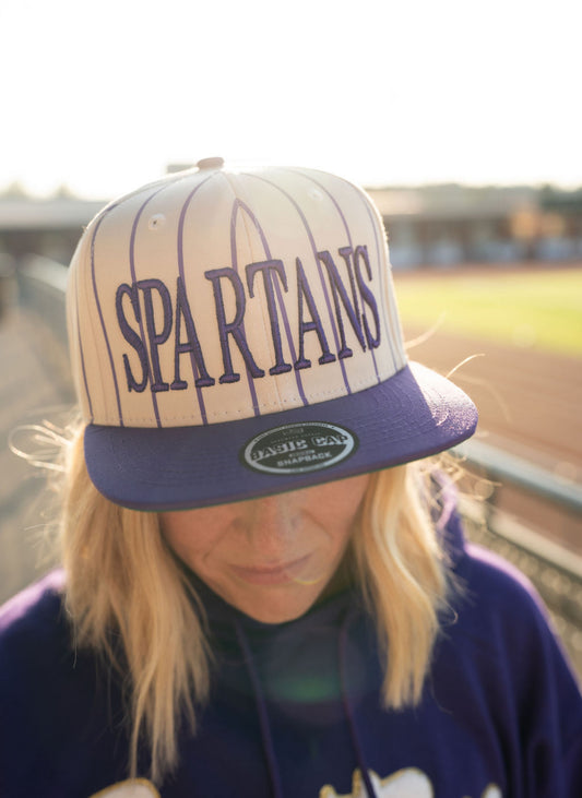 Thanks for the photo! Here's an updated Shopify description tailored specifically *

A total home run for Spartan fans! This vintage-inspired snapback features a bold **SPARTANS** front embroidery over classic purple pinstripes for that throwback ballpark vibe—because team spirit never goes out of style.

🟣 **Details:**

* Cream base with vertical **purple pinstripes**
* Bold **SPARTANS** embroidered across the front
* Purple