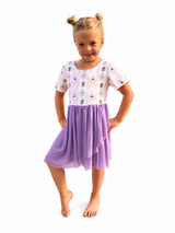 Girls Halloween twirl dress with a whimsical witch, pumpkin and spider print bodice, lavender purple tulle skirt, and short sleeves, modeled on a white studio background.