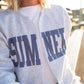 Absolutely! Here's the updated Shopify description with the correct color:

---

**Sumner Sweatshirt Cardigan – Women’s**

Show your local pride in comfort and style with our Sumner Sweatshirt Cardigan! This cozy layering piece features a classic varsity-style “SUMNER” graphic across the front in **bold purple lettering**, perfect for game days, school events, or everyday errands around town.

🟣 **Details:**

* Heather gray with **purple block lettering**
* Open-front cardigan style (no buttons or zippers)