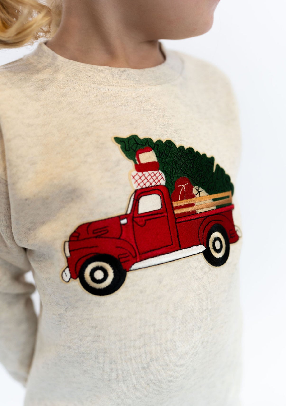 Beige sweater with a red truck and Christmas tree design on a white background