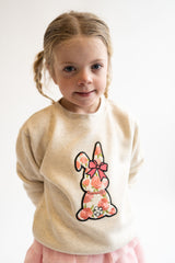 Young girl wearing a beige sweater with a floral bunny chenille patch on a white background