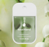 Touchland power mist hand sanitizer with green leaves and white flowers in the background