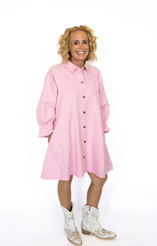 Turn heads with the sweetest sparkle in our Pink Veveret Rhinestone Denim Dress! This playful button-down style combines a soft blush denim with all-over rhinestone stripes for the perfect mix of feminine charm and everyday comfort.

✨ Details:

Light pink denim with shimmering vertical rhinestone accents

Button-down front for easy wear

Relaxed, slightly oversized fit for a flattering drape

Side pockets for function and style

3/4 length sleeves with ruffled elastic cuffs

Available in sizes S–L