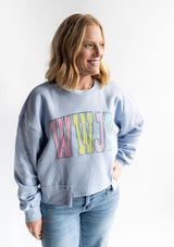Woman wearing light blue WWJD striped patch crewneck sweatshirt with colorful varsity style lettering