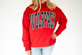 A person wearing a bright red sweatshirt with a large arched 'WOLFPACK' graphic across the chest in black and white, paired with light blue jeans, against a plain white background.