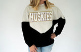 Huskies chenille varsity colorblock sweatshirt in heather gray and black with oversized white HUSKIES lettering outlined in purple and gold.