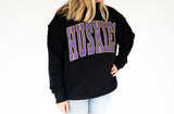 Women’s black Huskies mock neck sweatshirt featuring oversized purple and gold polka dot HUSKIES lettering, perfect for game day and tailgating.