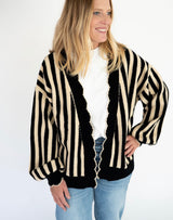 A woman wearing a black and cream striped knit cardigan over a white top and blue jeans, photographed against a plain light background.