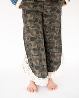 A woman wearing camouflage wide-leg pants with a white crochet lace hem, shown from the waist down against a plain white background.
