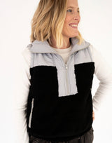 A woman wearing a color-block fleece vest with a black lower section, light gray upper section , over a white long-sleeve shirt, against a plain white background.