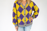 A woman wearing a purple and yellow argyle cardigan with gray trim and brown buttons, paired with light blue jeans, against a plain white background.